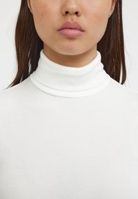 Hvid ribbet turtleneck bluse med høj krave, der har en tætsiddende pasform og glat tekstur. Ingen mønstre eller dekorationer synlige.