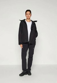 Must värvi välijakk, millel on kapuuts, lukuga kinnitus ja kaks küljetaskut. Koos mustade pükste ja mustade spordijalanõudega.