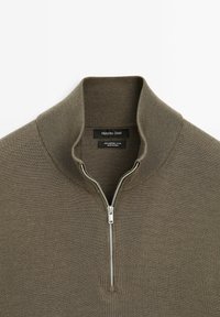 Merino wool pullover, olive green, features a zippered mock neck, ribbed texture, and a fitted design. Label visible inside with brand details.