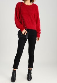 Czerwony, puszysty sweter z szerokim dekoltem, zestawiony z czarnymi obcisłymi jeansami. Całość uzupełnia czarna torebka na ramię i botki za kostkę.