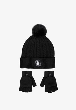 Cappello nero lavorato a maglia con pon pon e toppa, abbinato a guanti neri senza dita con dettaglio a bottone. Tessitura a trecce su tutta la superficie.