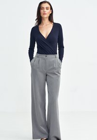 Granatowy długi rękaw kopertowy top sparowany z szarymi spodniami o wysokim stanie z plisami, charakteryzującymi się gładką teksturą i szerokimi nogawkami. Czarne obuwie dopełnia całość.