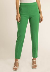 Pantalons verts ajustés avec une texture lisse, taille haute et sans fermeture visible. Associés à des talons blancs à lanières.