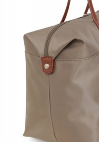 Sac fourre-tout beige avec une finition mate, doté d'une fermeture éclair, d'accents en cuir marron et d'une forme carrée, présentant une texture lisse et des coutures robustes.