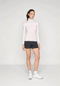 Šviesiai rožinė ilgos rankovės zip-up palaidinė su atspindinčiomis juostelėmis, derinama su juodais sportiniais šortais. Modelis vilki baltus sportinius batelius ir kulkšninius sokus.