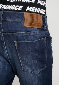 Dark blue denim jeans with a textured brown leather patch featuring perforations, branded “ANTONY MORATO,” and silver hardware on pockets.