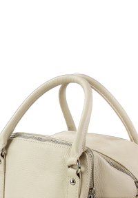 Crèmekleurige leren handtas met een korrelige structuur, twee ronde handvatten, een ritssluiting aan de bovenzijde en zilverkleurige metalen accenten.