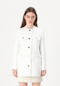 White tweed jacket with metallic buttons, textured fabric, two front pockets, and a high neckline. Features a straight cut and long sleeves.