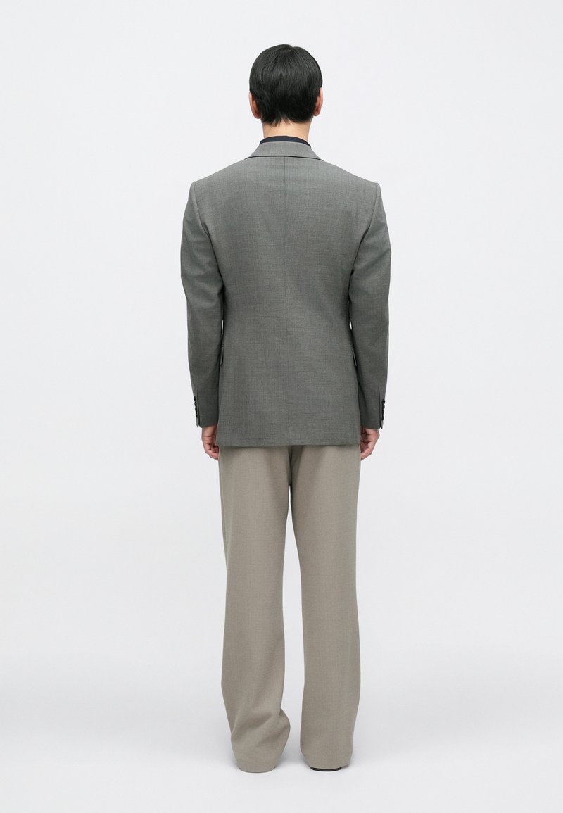 Gray suit jacket with structured shoulders, peak lapels, and two buttons, paired with light beige wide-leg trousers, viewed from the back.