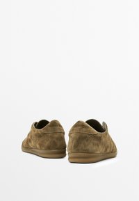 Scarpe in suede marrone con profilo basso, punta arrotondata e design minimalista. Texture morbida e suola in gomma per il comfort.