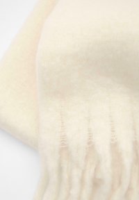 Sciarpa color crema realizzata in morbido tessuto spazzolato, con una superficie testurizzata e bordi frangiati per un tocco di dettaglio in più.