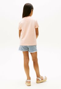 Lyserød bomulds t-shirt parret med blå og hvide stribede denimshorts med frynset kant. Båret med hvide sandaler på en struktureret sål.