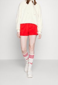 Krämfärgad fluffig tröja med rosett, röda shorts och vita knästrumpor med röda ränder, i kombination med ljusa sneakers. Enkelt design.