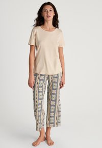 Top corto a maniche corte color beige chiaro abbinato a pantaloni larghi con fantasie floreali e geometriche nei toni del blu, giallo e verde.