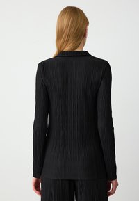 Zwarte geplooide lange mouwen jas met een kraag, voorzien van verticale textuurlijnen en een rechte snit, in combinatie met bijpassende broek.