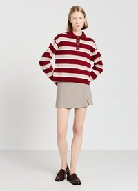 Gestreiftes Strick-Polo in Rot und Beige mit Knopfleiste, kombiniert mit einem hellbeigen Rock und dunkelbraunen Loafers.