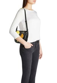 Borsa a tracolla nera con accenti gialli e arancioni, con design di personaggio a cartone animato e tracolla removibile. Texture in pelle liscia.