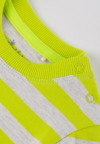 Grüner und grauer gestreifter Stoff mit einem ribbelten Kragen. Verfügt über Druckknöpfe und eine glatte Textur. Nahaufnahme der Details am Kragen.