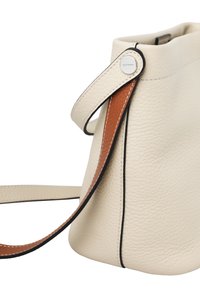 Kremfarvet lædertaske med en tekstureret overflade, udstyret med en brun læderrem og sorte kantsting for kontrast. Enkel, rundet design.