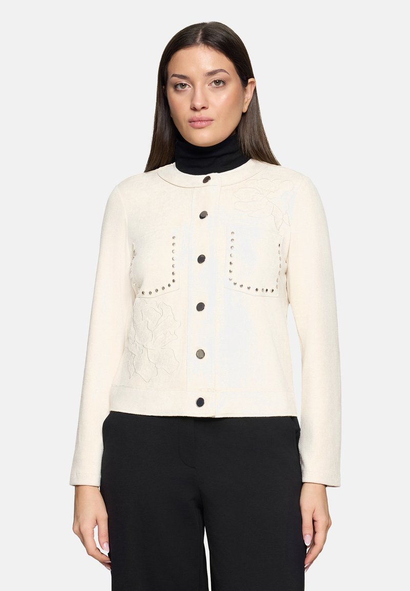 Veste ivoire à manches longues, dotée de deux poches poitrine, de clous métalliques décoratifs et d'un embossage floral sur le côté gauche.