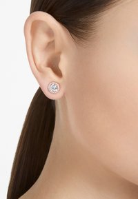 Náušnice ve tvaru kruhu z růžového zlata, s velkým středovým krystalem obklopeným menšími čirými kameny v kulatém závěsu.