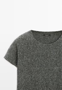 Szara krótka koszula z wełny z zaokrąglonym dekoltem, wykonana z miękkiego, teksturowanego materiału z subtelnymi, cętkowanymi detalami. Widoczna metka marki.