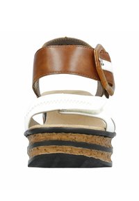 Witte en bruine wedge sandaal met een brede bruine band, verstelbare gesp, kurkachtige middenzool en gestructureerde zwarte buitenzool.