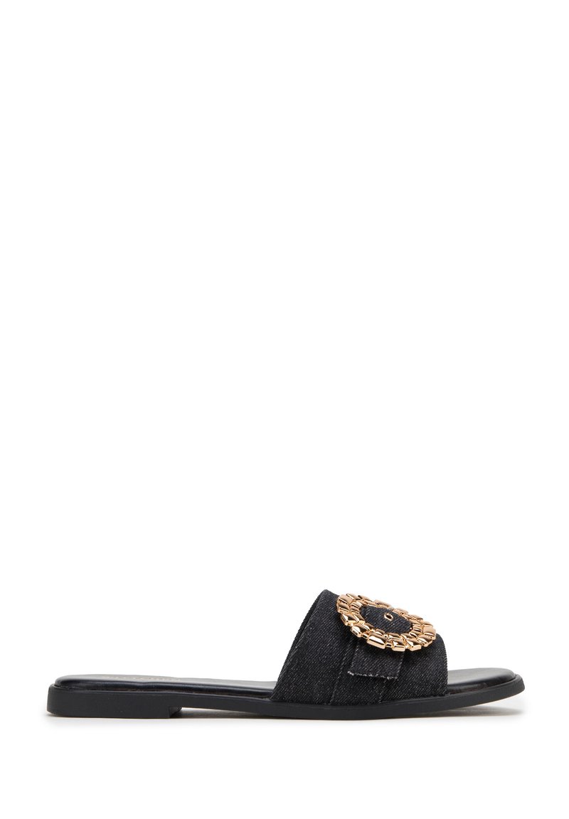 Zwarte denim slide sandaal met een ronde goudkleurige kettingaccent op de bovenkant en een platte zwarte zool. Eenvoudig, open-tenontwerp.