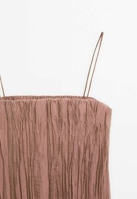 Haut à bretelles spaghetti de couleur rose poudrée avec une texture froissée et un décolleté droit sur un fond blanc.