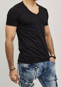 T-shirt noir à manches courtes et décolleté en V, fabriqué en tissu doux. Porté avec un jean en denim bleu délavé, présentant des détails de poches et des accents en métal.