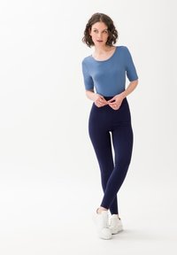 Niebieski prążkowany top i granatowe legginsy, oba wykonane z elastycznego materiału. Strój uzupełniają białe trampki na jasnym tle.