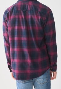 Camisa de franela de cuadros en azul oscuro y rosa. Manga larga con puños abotonados, dobladillo curvado y detalle en la yugo trasero. Textura suave.