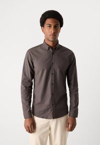 Cămașă button-up, cu mâneci lungi, de culoare brown închis, cu guler, având o textură netedă și detalii cu nasturi. Port cu pantaloni de culoare deschisă.