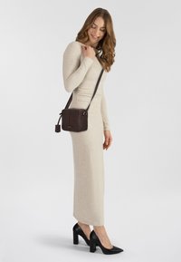 Abito beige a maniche lunghe con lavorazione a coste e silhouette aderente, abbinato a una piccola borsa testurizzata marrone scuro e a scarpe nere con tacco alto.