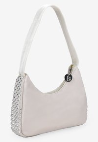 Bolso de mano de color beige claro, hecho de material suave, con cierre de cremallera, una correa corta y un lateral adornado con tachuelas plateadas.