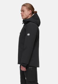 Black waterproof jacket with a hood, featuring a zipper, elastic cuffs, and a circular logo on the sleeve. Smooth texture and modern design.