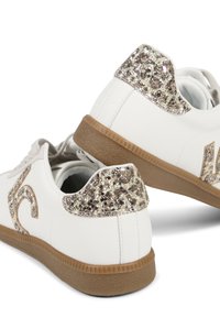 Zapatillas de cuero blancas con una suela de goma texturizada color marrón y un superpósito de purpurina dorada en el talón. Presenta un logo decorativo en el lateral.