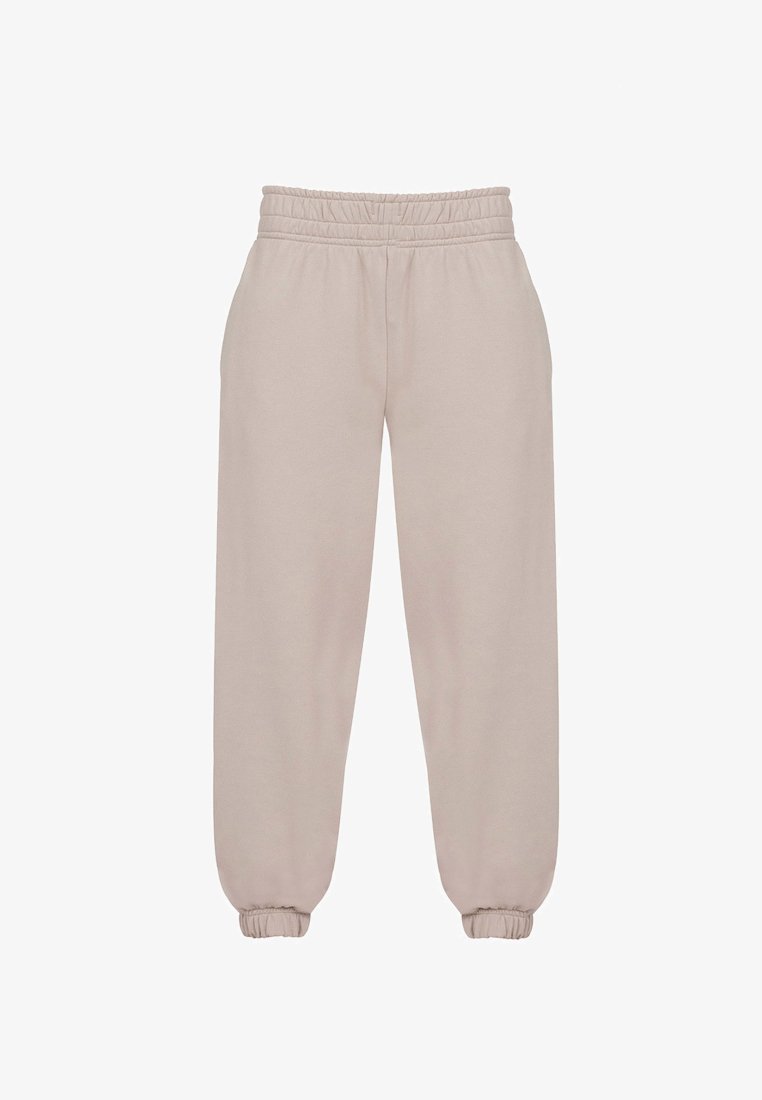 Beżowe spodnie dresowe wykonane z miękkiego materiału, z elastycznym paskiem w talii, zakończone ściągaczami na kostkach i luźnym krojem dla wygody.
