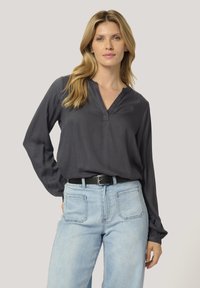 Dark gray long-sleeve blouse with a V-neckline, made of smooth fabric. Paired with light blue high-waisted jeans and a black belt.