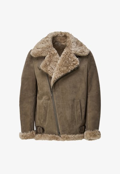 Shearling jas in taupe, met een brede bontkraag, zijrits en gespsluitingen bij de manchetten en zoom. Zachte textuur overal.