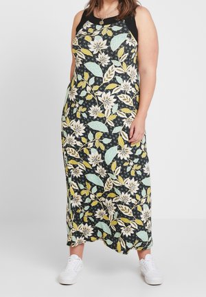 Robe maxi sans manches avec partie supérieure noire et grand motif floral en vert pastel, jaune et blanc, portée avec des baskets blanches.