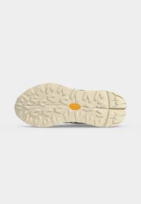 Semelle de chaussure beige avec des crampons profonds et anguleux et un logo Vibram orange au centre sur un fond blanc uni.