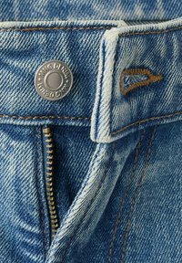 Gros plan sur la fermeture éclair et le bouton en métal d'un jean en denim bleu avec le nom de la marque "KING DENIM" brodé sur la boucle de ceinture et des détails en fil orange.