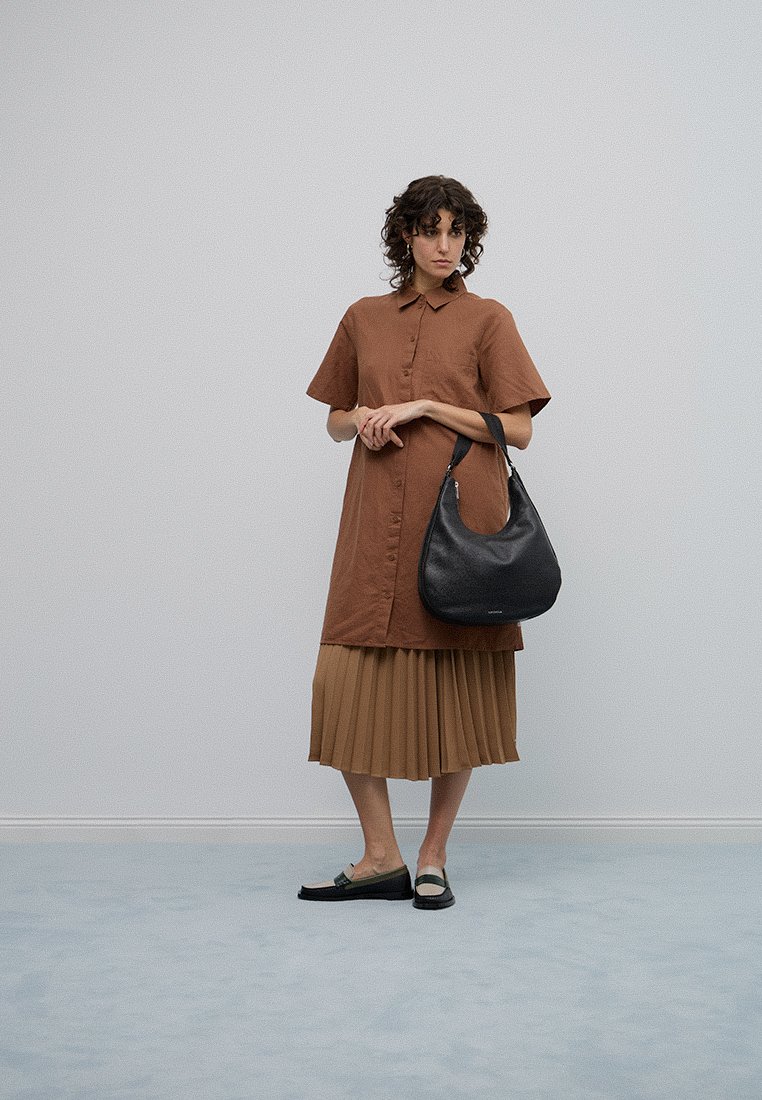 Robe chemise marron à boutons, jupe beige plissée, sac à bandoulière noir et chaussures plates noires avec des accents verts. Design simple et élégant.