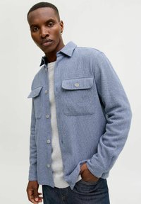 Bl�å teksturert skjortejakke med to brystlommer, knappelukking foran og krage, kombinert med en lys grå genser.