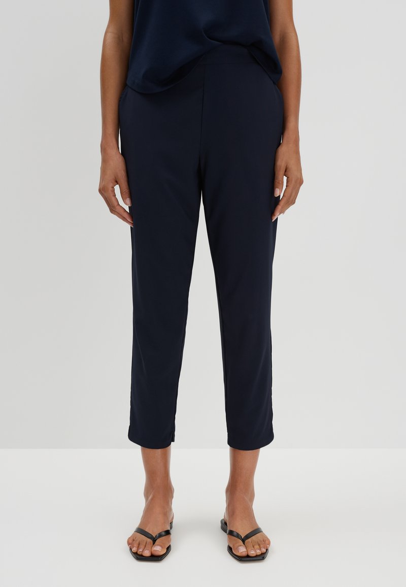 Pantalons cropped navy en tissu lisse et léger. Dotés d'une taille plate et de poches latérales. Associés à des tongs noires.