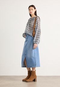 Denim pitkä hame, jossa on etureikä, yhdistettynä ruudulliseen paitaan, jossa on kerättyjä hihoja. Ruskeat mokkanahkaiset nilkkurit, joissa on lohkare korkoa.