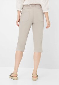 Pantaloni capri beige con vestibilità slim, dotati di risvolti e due tasche posteriori. Il materiale sembra essere una miscela di cotone leggera.