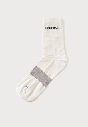 Biela športová ponožka so sivým pásikom cez klenbu a slovom "sportful" čiernym písmom blízko lemu.