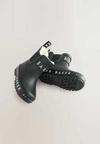 Bottes noires en caoutchouc jusqu'aux chevilles avec une doublure blanche douce, présentant des semelles texturées et une marque imprimée blanche sur les côtés et le talon.